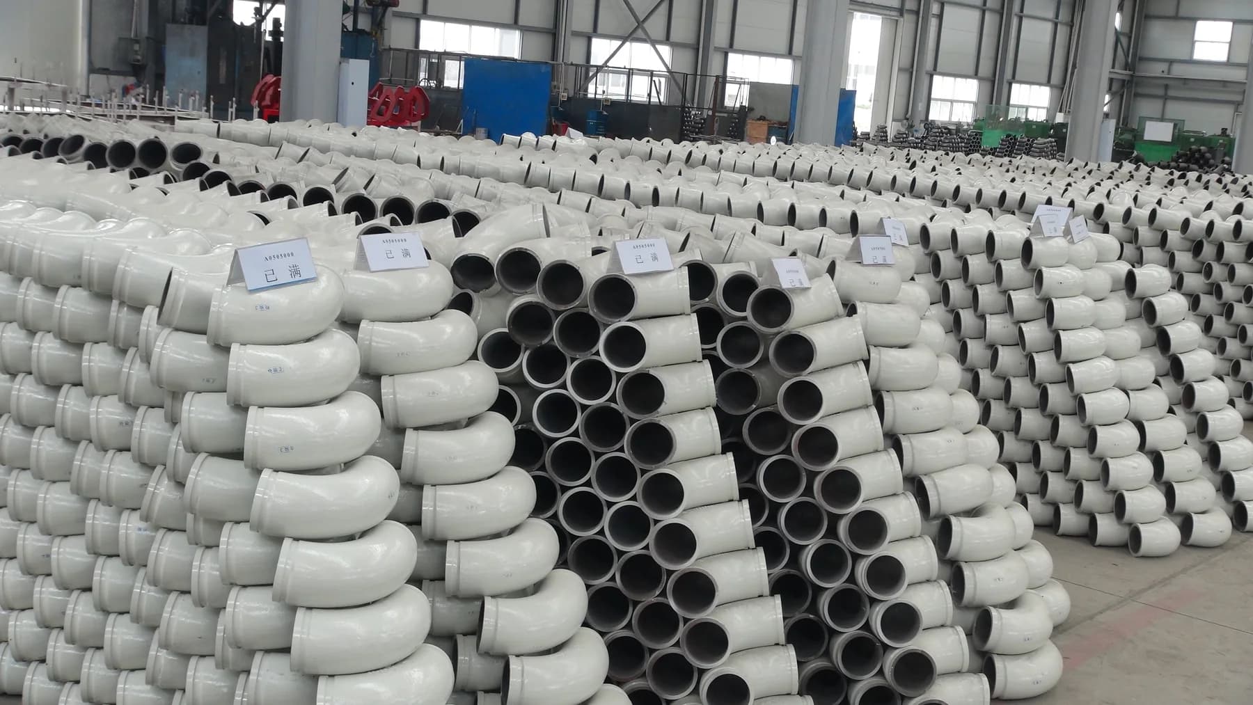 Bainitic steel wear elbows and straight pipe stacked on the production floor